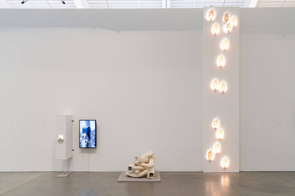Installation view of an installation featuring plugin lights that resemble small fires, video monitors, and other objects.